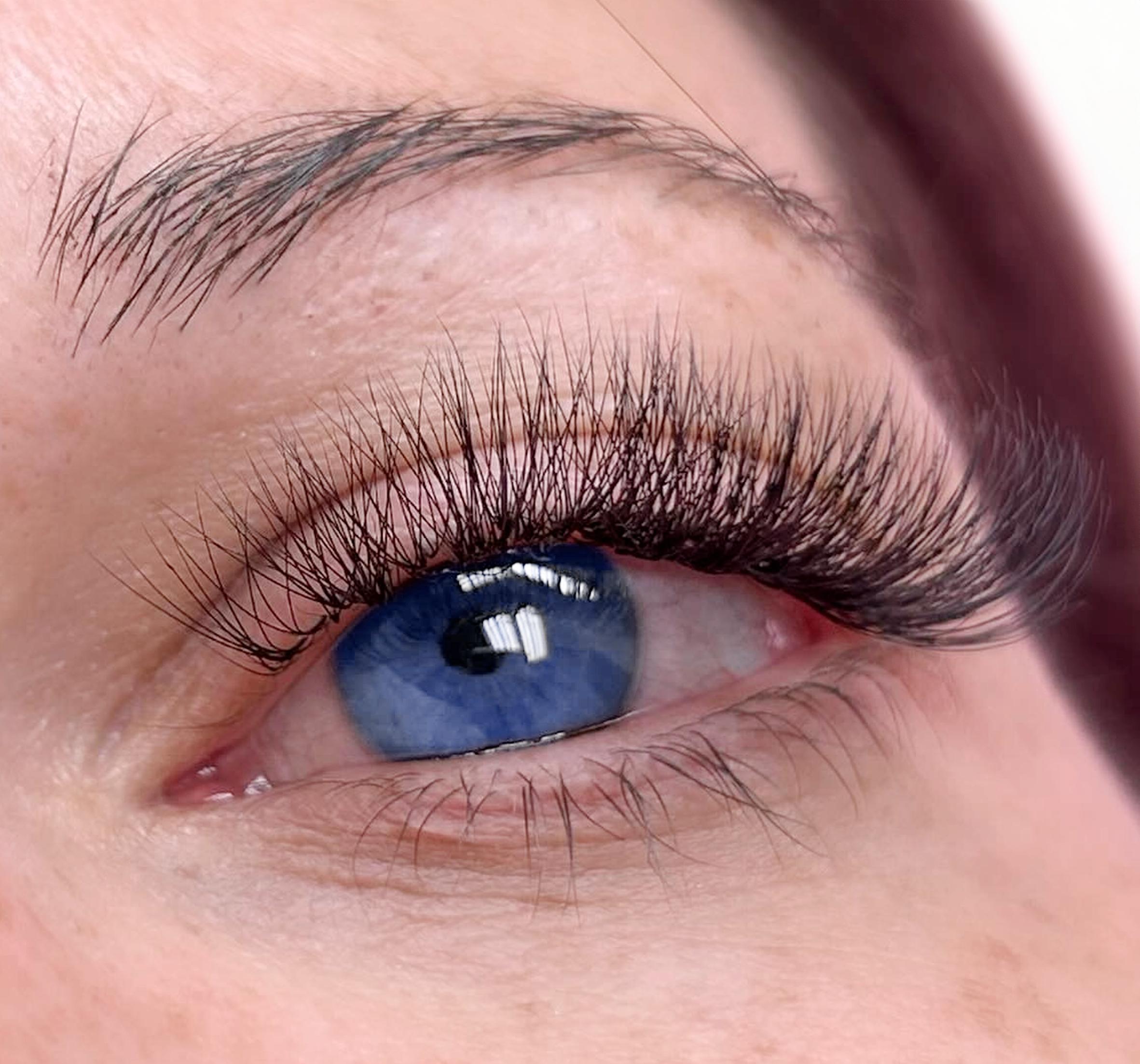 Macro close-up of a full set of natural-to-medium lash extensions on a blue eye — real work by US Nails